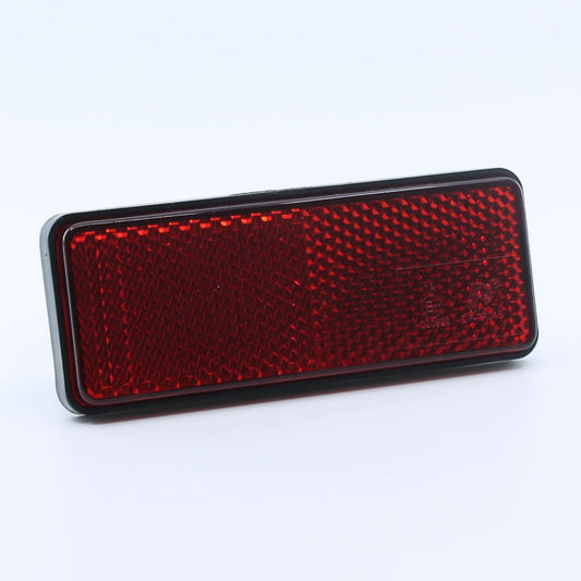 Reflector de seguridad de forma rectangular, color rojo, para montaje trasero con fijación adhesiva, utilizado en remolques y maquinaria agrícola.