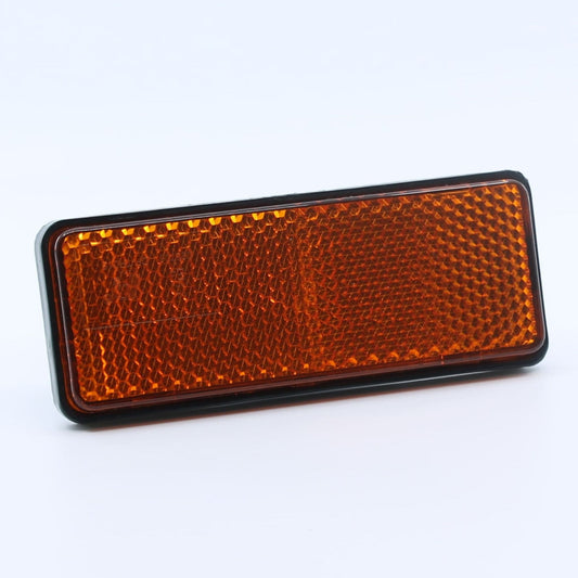 Reflector de seguridad de forma rectangular y color ámbar (naranja), para montaje lateral con fijación adhesiva, utilizado en remolques y maquinaria agrícola.