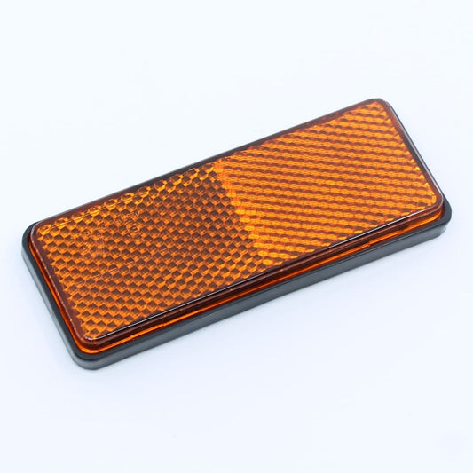 Reflector de seguridad de forma rectangular y color ámbar (naranja), para montaje lateral con fijación adhesiva, utilizado en remolques y maquinaria agrícola.