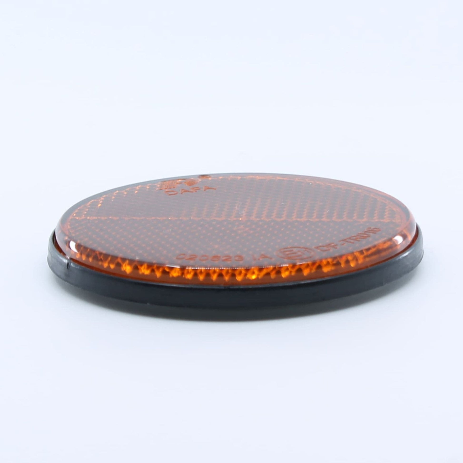 Reflector de seguridad de forma redonda y color ámbar (naranja), para montaje lateral con fijación adhesiva, utilizado en remolques y maquinaria agrícola.