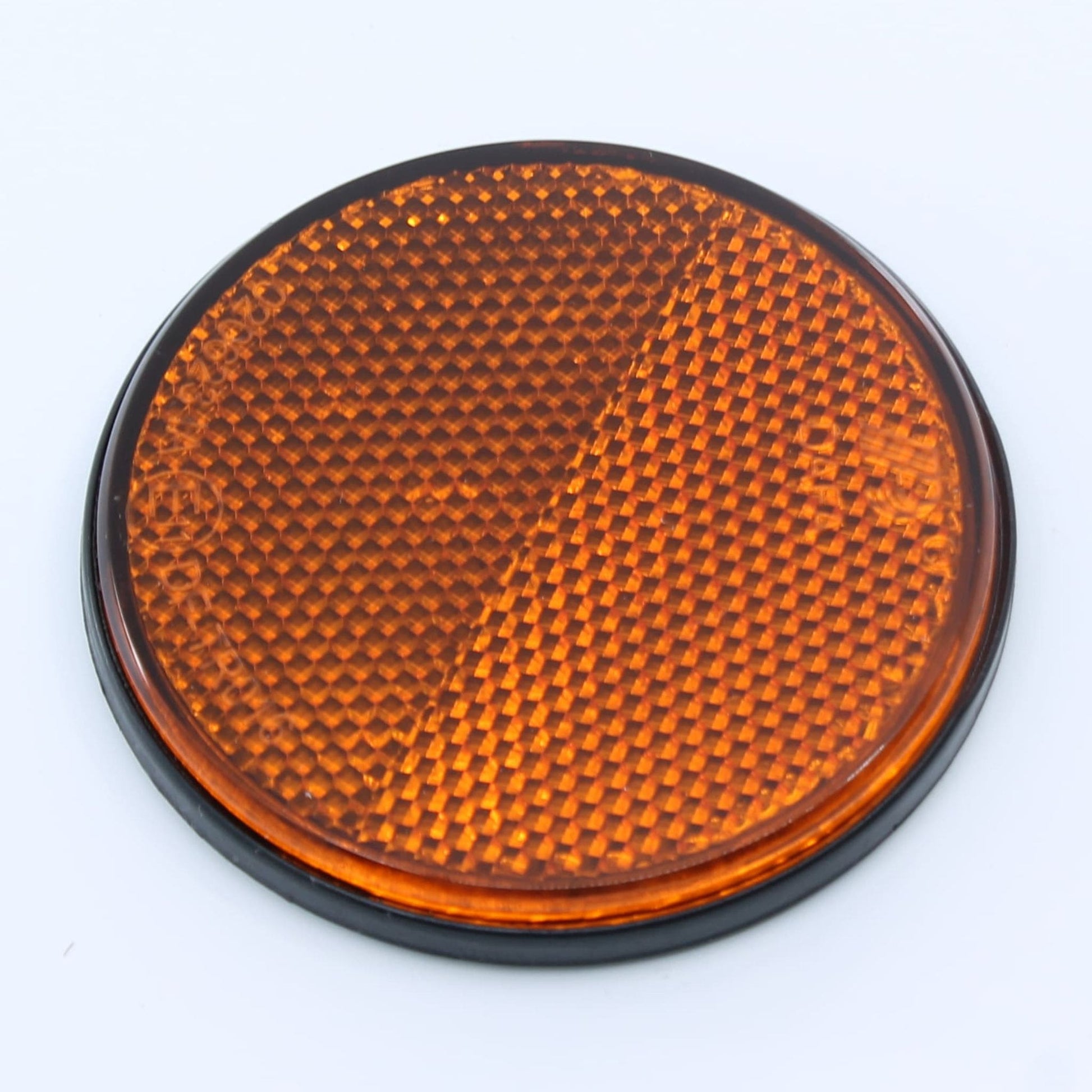 Reflector de seguridad de forma redonda y color ámbar (naranja), para montaje lateral con fijación adhesiva, utilizado en remolques y maquinaria agrícola.